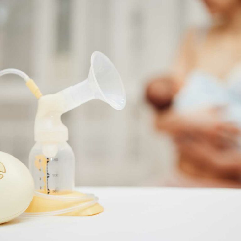 Photo of breast pump in foreground, with a mom & baby out of focus in background.