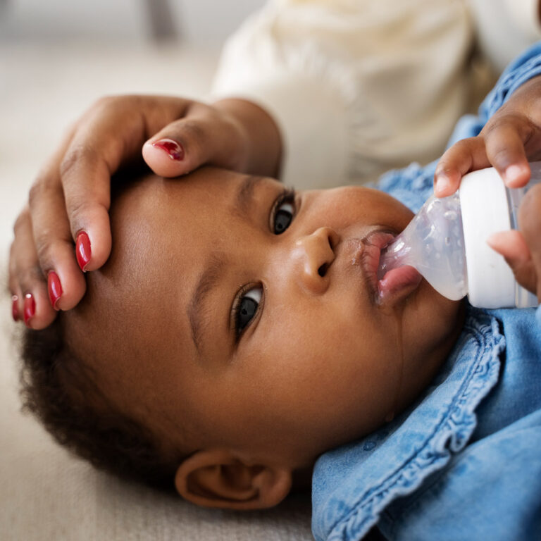 African American baby drinking from a bottle while a mother's hand cradles the baby's head